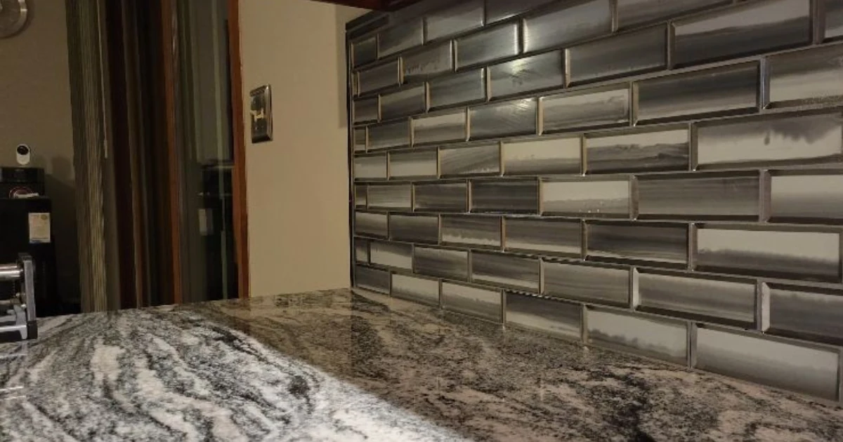 Close view of a patterned stone countertop and gray glass-tile backsplash