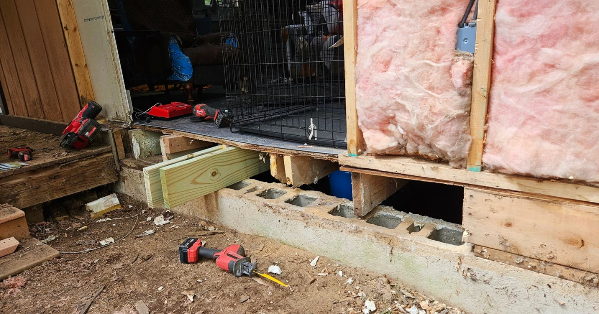 Front wall opened for rot repairs, showing framing, insulation and the area beneath the doorway